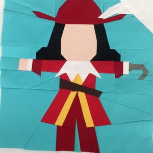 May include: A paper pieced quilt block featuring a cartoon pirate with a red hat, black hair, a red and yellow jacket, and a brown belt. The pirate is holding a hook in his right hand. The background is turquoise.