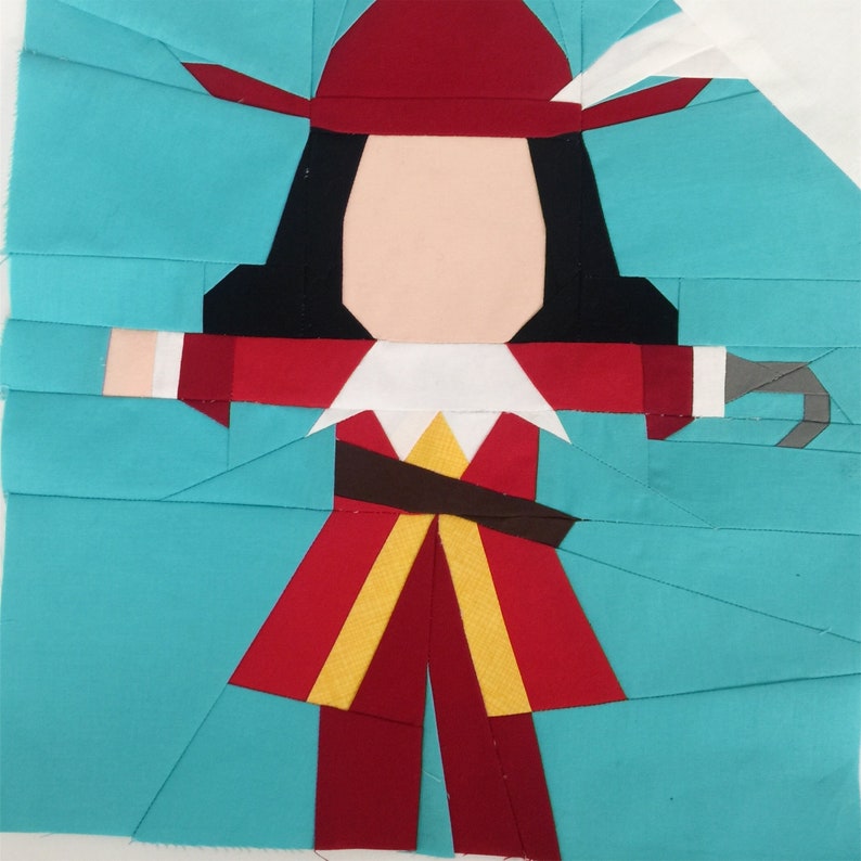 May include: A paper pieced quilt block featuring a cartoon pirate with a red hat, black hair, a red and yellow jacket, and a brown belt. The pirate is holding a hook in his right hand. The background is turquoise.