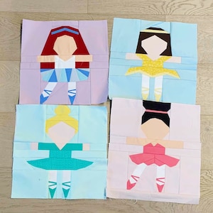 May include: Four colorful paper pieced ballerina figures. Each figure is a different color and has a different hair color and style. The figures are on a light wood background.