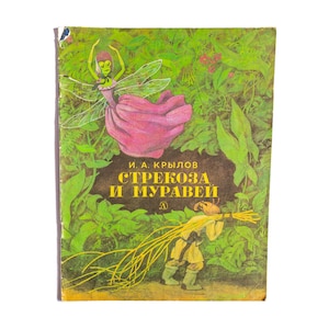 Puede incluir: Una portada de libro vintage con una libélula verde con vestido rosa y una hormiga marrón cargando palos amarillos. El texto dice I. A. KRYLOV STREKOZA I MURAVEI en amarillo sobre un fondo marrón oscuro, rodeado de follaje verde.