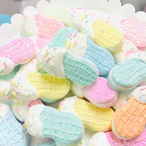 Könnte beinhalten: Eine Sammlung von pastellfarbenen Flip-Flops in Form von Eiswaffeln mit weißem Frosting und Streuseln.