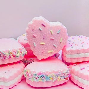 May include: A stack of pink heart-shaped cookies with white frosting and colorful sprinkles.