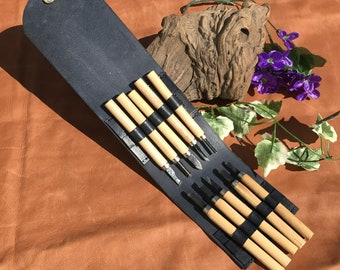 May include: A black leather roll-up case with eight wood carving tools. The tools have black handles and are arranged in the case.