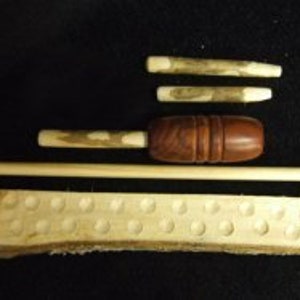 May include: A wooden game set with a long wooden stick, a wooden mallet, three wooden sticks with pointed ends, and a wooden board with 20 holes.