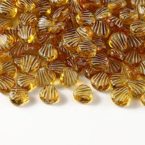 May include: A collection of small, translucent amber-colored glass beads shaped like seashells. Each bead features a series of raised, white, linear ridges radiating from the base to the outer edge, creating a textured, fan-like appearance.