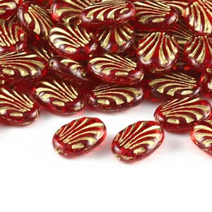 Könnte beinhalten: Eine Ansammlung ovaler Glasperlen in einer durchscheinenden tiefroten Farbe. Jede Perle weist auf der Oberfläche ein erhabenes, metallisch goldfarbenes muschelartiges Muster auf. Die Perlen sind in einem losen Haufen angeordnet und zeigen ihre glatten Kanten.