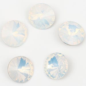 May include: Five iridescent, round crystal rhinestones with a faceted design are arranged on a white background. The crystals have a pearlescent sheen, reflecting shades of blue and white. These decorative embellishments are ideal for crafts.