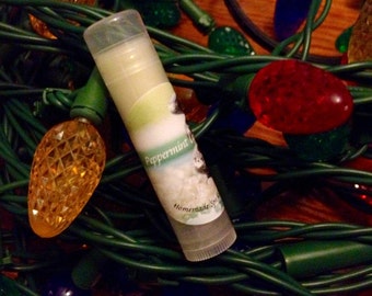 May include: A clear tube of peppermint lip balm with a green and white label that says "Peppermint Lip Balm" and "Homemade Special". The lip balm is surrounded by green and red Christmas lights.