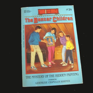 May include: The Mystery of the Hidden Painting book cover, featuring a group of children in an attic, holding a framed portrait. The book is part of the "The Boxcar Children" series, created by Gertrude Chandler Warner.