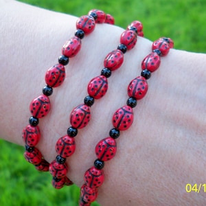 May include: Three layered bracelets made of red and black beads. Each bead is shaped like a ladybug with black spots.