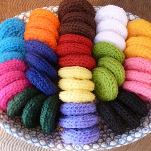 May include: A woven basket filled with stacks of colorful, knitted coasters. The coasters are in various colors, including blue, orange, brown, red, white, green, yellow, pink, and black. The basket has a white and blue patterned rim.