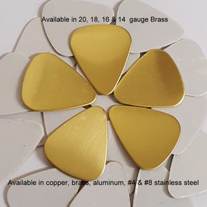 May include: A close-up of six gold guitar picks arranged in a circle. The text "Available in 20, 18, 16 & 14 gauge Brass" is at the top of the image. The text "Available in copper, brass, aluminum, #4 & #8 stainless steel" is at the bottom of the image.