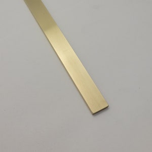 May include: A rectangular, gold-colored metal bar. The bar is straight with a matte finish and is positioned diagonally against a white background. The bar appears to be made of brass or a similar alloy.