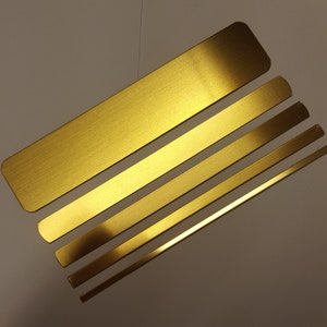 May include: Five gold-colored metal strips of varying lengths, arranged in a diagonal pattern on a white background.