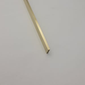 May include: A single, elongated, gold-colored metal bar with a rectangular cross-section. The bar is positioned diagonally against a white background, showcasing its polished surface and sharp edges. The bar's length is approximately 12 inches.