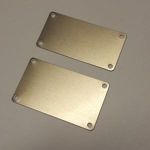 May include: Two rectangular metal plates with rounded corners and four holes in each. The plates are a brushed gold color.