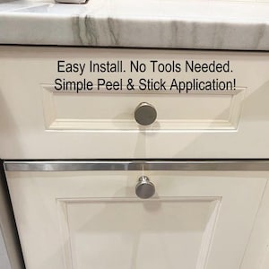 May include: Close-up of two off-white cabinet drawers with silver hardware. The top drawer has a round knob, and the bottom drawer has a similar knob. The text "Easy Install. No Tools Needed. Simple Peel & Stick Application!" is printed above the drawers.