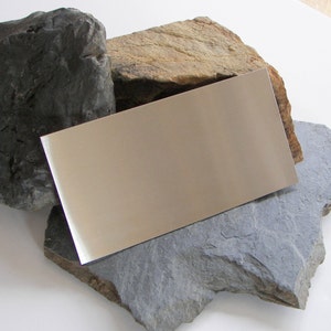 May include: A rectangular piece of polished metal with a reflective surface, resting on top of three different coloured rocks.