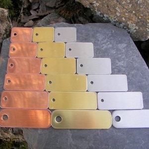May include: A set of ten rectangular metal tags in various sizes. The tags are made of copper, brass, and nickel. The tags have a hole at the top for attaching to a key ring or other item.