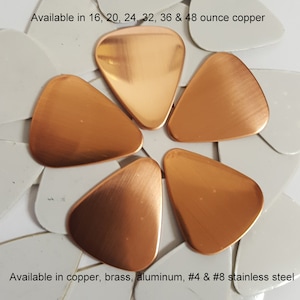May include: A close-up of six copper guitar picks in a variety of sizes. The picks are arranged in a flower shape on a white background. The text "Available in 16, 20, 24, 32, 36 & 48 ounce copper" is at the top of the image. The text "Available in copper, brass, aluminum, #4 & #8 stainless steel" is at the bottom of the image.