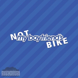 Op de afbeelding: Witte vinyl sticker met de tekst "NOT my boyfriend's BIKE" op een blauw-wit gestreepte achtergrond.