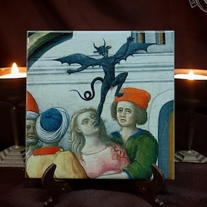 Op de afbeelding: Vierkante tegel met een middeleeuws schilderij van een donkere duivelsfiguur met vleermuisvleugels, zwevend boven een groep mensen. Het kunstwerk heeft een vintage esthetiek, met gedempte kleuren en een historisch thema. De tegel wordt op een kleine standaard getoond.