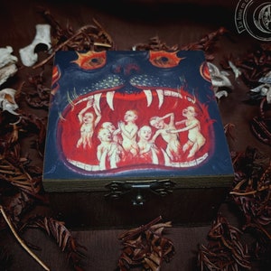 May include: A wooden box with a hinged lid. The lid features a painting of a monstrous mouth with rows of sharp teeth. Inside the mouth are several small figures with outstretched arms. The box is decorated with a metal clasp.