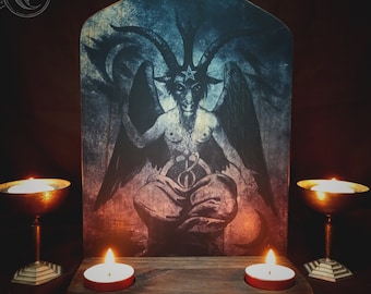 May include: A dark wooden altar with four candles, two on each side of a framed image of a horned figure with wings. The image is on a dark blue and red background.