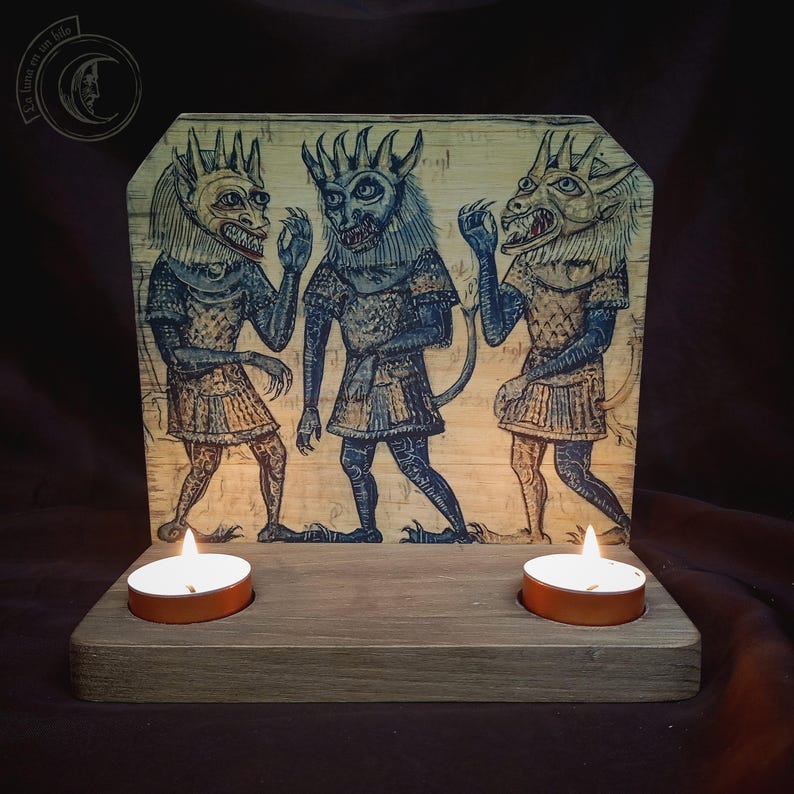 K&ouml;nnte beinhalten: Holzkerzenhalter mit einem bemalten Panel, das drei d&auml;monische Figuren zeigt. Die Figuren sind blau, beige und goldfarben, mit H&ouml;rnern und Schw&auml;nzen. Zwei brennende Teelichter befinden sich vor dem Panel.