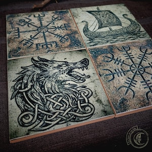 May include: Set of four square ceramic tiles with Viking-themed designs. Each tile features a different black and white illustration: a Viking ship, a wolf, and two different runic symbols. The tiles have a distressed, aged appearance.