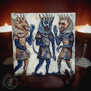 May include: Square tile featuring a medieval illustration of three demonic figures with horns, claws, and blue and tan clothing. The figures are set against a parchment-like background. The tile is displayed on a dark surface.
