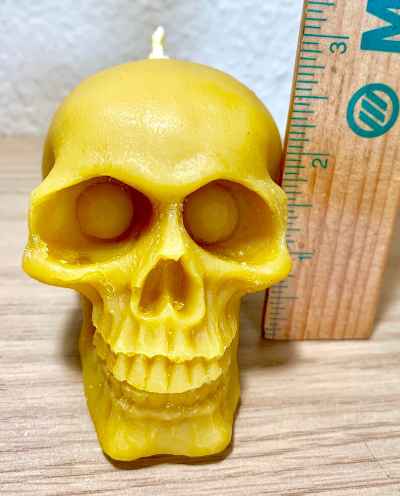 May include: A yellow beeswax skull candle with a small wick on top. The candle is about 3 inches tall.