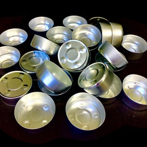 May include: A pile of silver-colored metal tea light candle holders. The holders are round and have a small lip around the top edge.