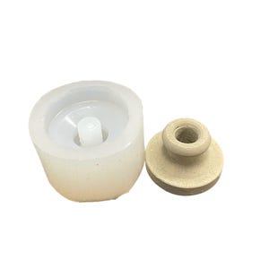 May include: A white silicone mold for making a small bottle with a wooden stopper. The mold is round and has a small hole in the center for the stopper.