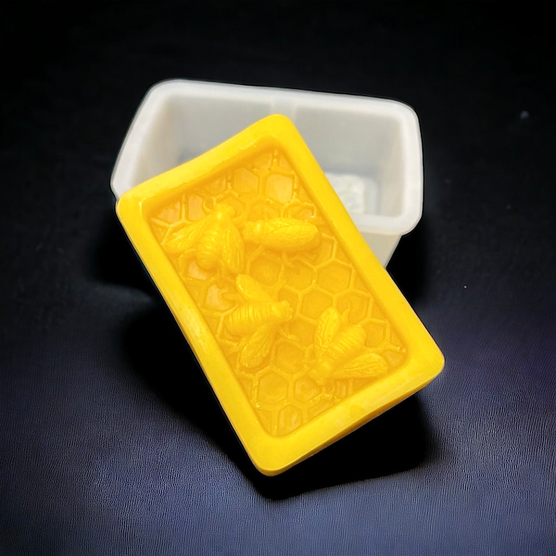 May include: A yellow silicone mold for making soap. The mold features a honeycomb design with three bees in relief.