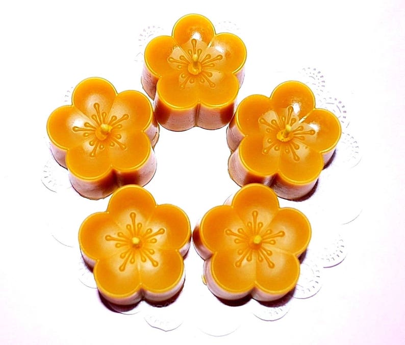 May include: Five small, yellow, wax candles shaped like flowers. The candles have a five-petal design and a small wick in the center of each flower.