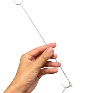 May include: A silver metal tool with a loop at the top and a hook at the bottom. A white string is attached to the hook.