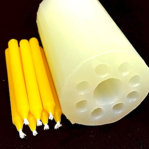 Op de afbeelding: Een witte siliconen mal met acht ronde holtes voor het maken van kaarsen. De mal ligt naast een bundel van zes gele kaarsen.
