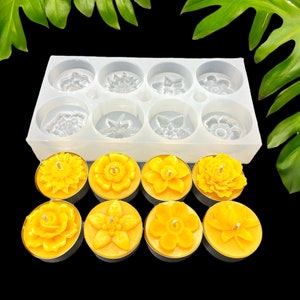 Könnte beinhalten: Eine Silikonform mit acht Blumenmustern zum Herstellen von Teelichtern. Die Form ist mit acht fertigen Kerzen gezeigt, jede mit einem anderen Blumenmuster.