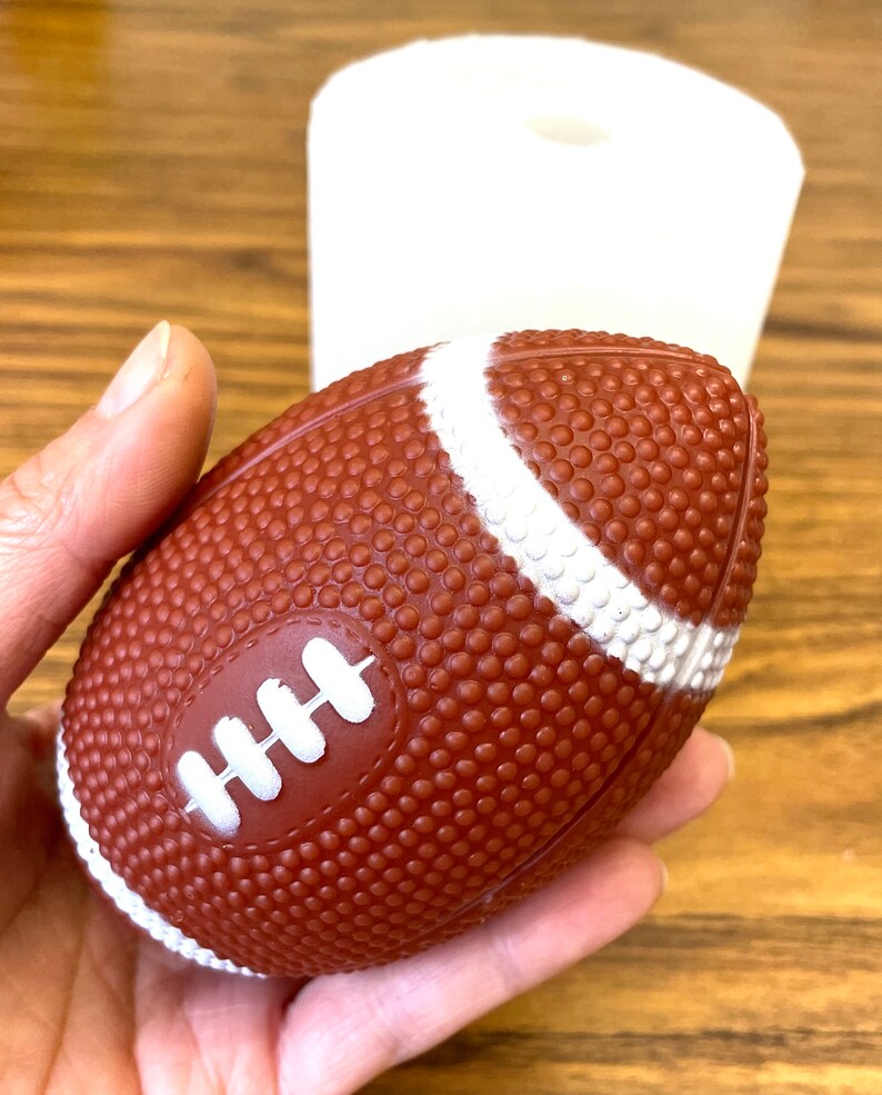 K&ouml;nnte beinhalten: Ein brauner und wei&szlig;er Fu&szlig;ball mit Schn&uuml;rsenkeln. Der Fu&szlig;ball ist aus einem strukturierten Material.