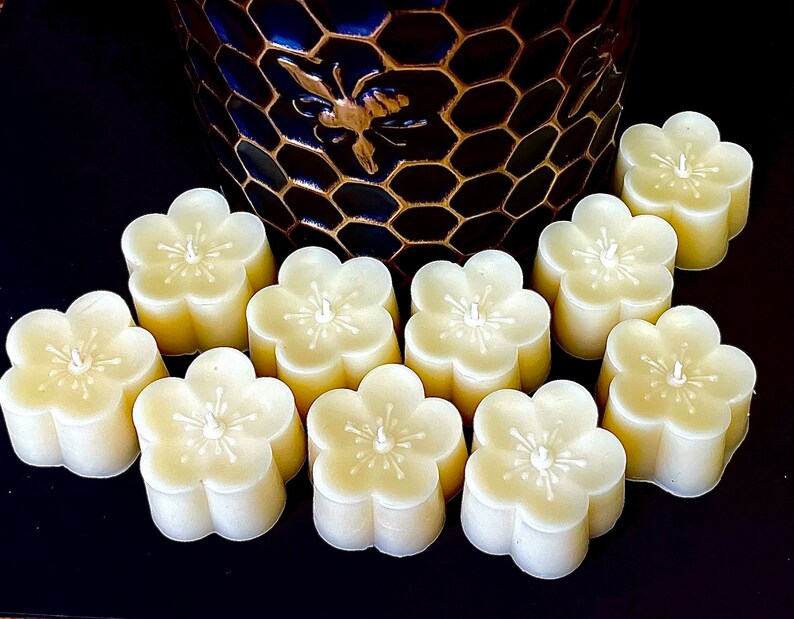 May include: Ten small, white, flower-shaped candles with a raised center. The candles are arranged in a semi-circle on a black surface.