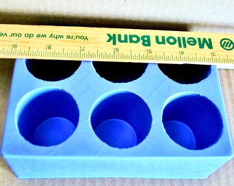 May include: A blue silicone mould with six round cavities. The mould is sitting on a brown surface. A wooden ruler with the text "Mellon Bank" is placed on top of the mould.