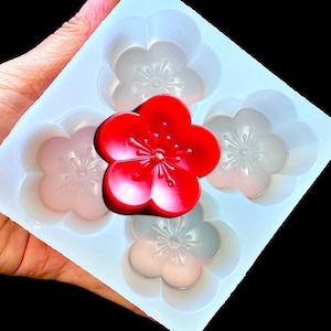 May include: A silicone mold with four flower-shaped cavities. A red flower-shaped candle is sitting on top of the mold.