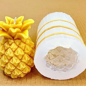 Puede incluir: Una vela amarilla con forma de piña y un molde de silicona blanco para hacer velas. El molde tiene una superficie texturizada y está diseñado para crear una vela con forma de piña.