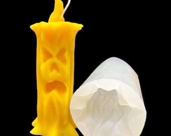 Puede incluir: Una vela amarilla con una cara tallada y una mecha blanca. La vela está en un molde de silicona transparente con una cara tallada.