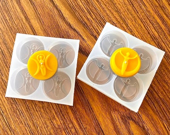 May include: Two silicone molds for making candles. The molds are clear and have a design of a woman with a crescent moon on each side. One mold has a yellow candle in it.