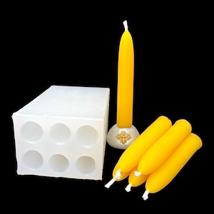 Könnte beinhalten: Eine Sammlung von Kerzenherstellungsartikeln vor schwarzem Hintergrund. Enthält eine weiße Silikonform mit sechs kreisförmigen Hohlräumen, mehrere gelbe Kerzen und eine einzelne Kerze in einem dekorativen Halter. Die Kerzen sind leuchtend gelb.