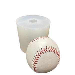 May include: A white silicone mold for making a baseball. The mold is cylindrical with a round opening at the top. A white baseball with red stitching is sitting next to the mold.