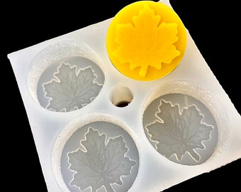Puede incluir: Un molde de silicona blanco con cuatro cavidades en forma de hoja. El molde está diseñado para hacer manualidades de resina. Una hoja de resina amarilla se muestra en la parte superior del molde.