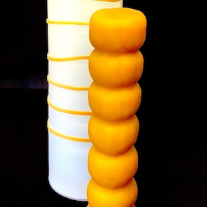 以下が含まれることがあります： 黄色い蜜蝋のろうそくで、ユニークなセグメントデザインが施されています。ろうそくは白いシリコンモールドの隣に置かれています。